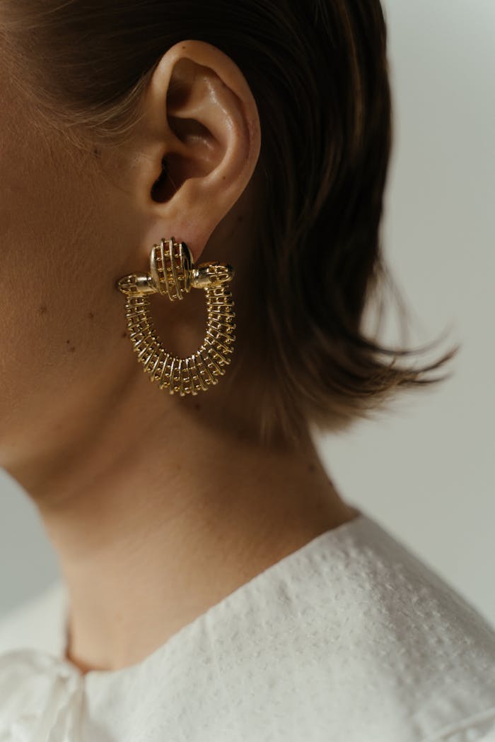 Stylish gold earring on a woman's ear against a soft background.